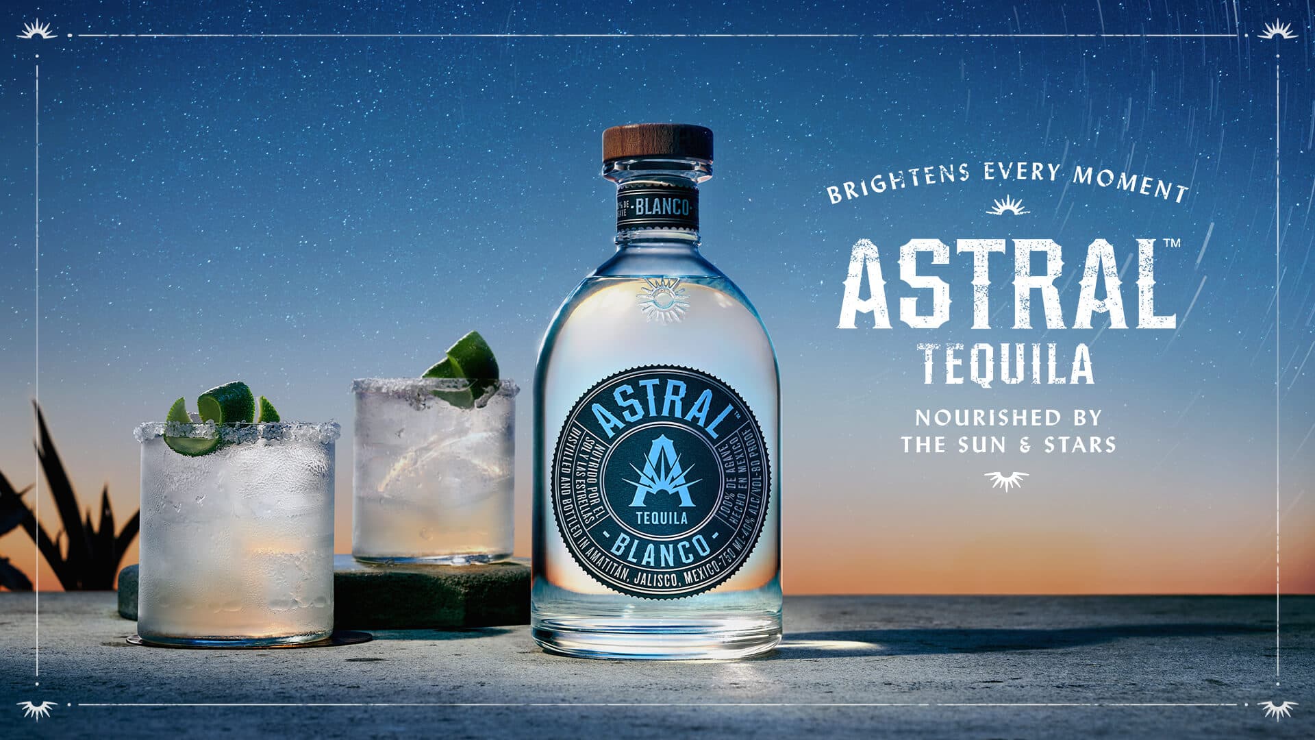 Bottle of Astral Tequila with two glasses filled with drinks to the side 